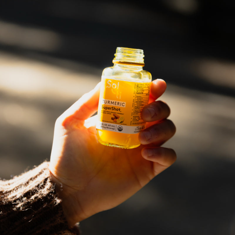 A hand holding a glass bottle of TURMERIC SuperShot in sunlight