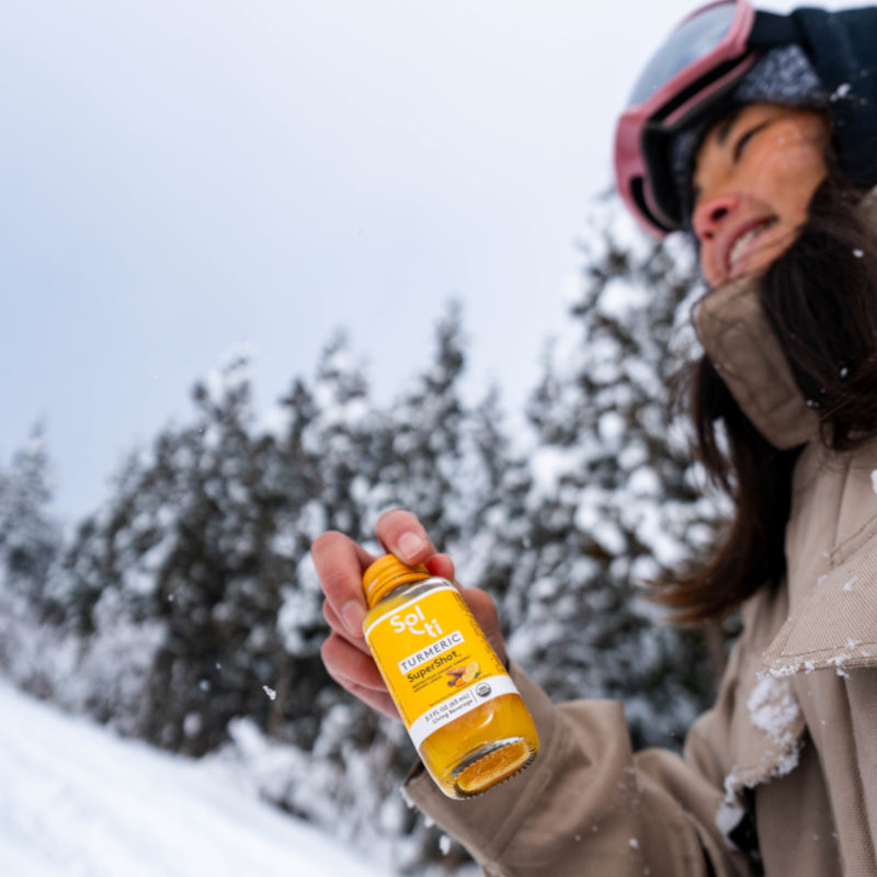 Sol-ti TURMERIC SuperShot bottle held outdoors in snow, angled label, winter background