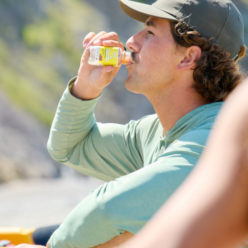 Person with green sweater drinking Sol-ti IMMUNI-TI SuperShot, angled label, outdoor background