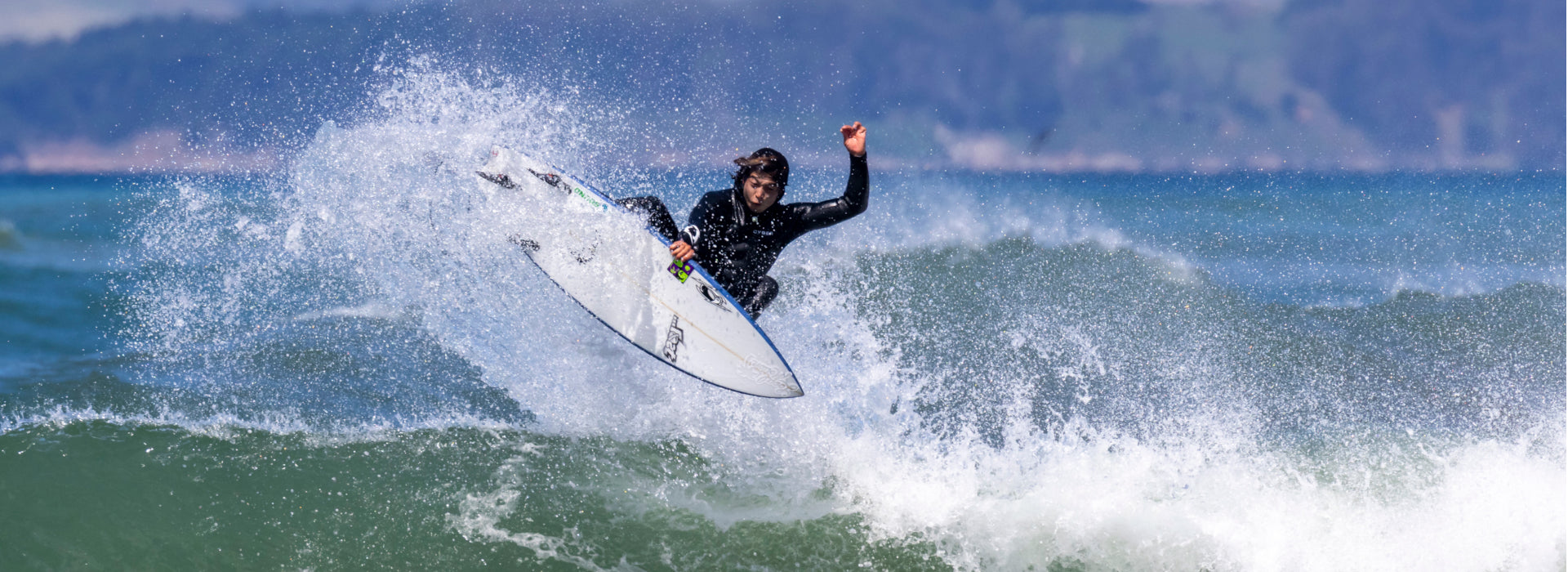 Surfer in a wetsuit riding a wave with mountains in the background