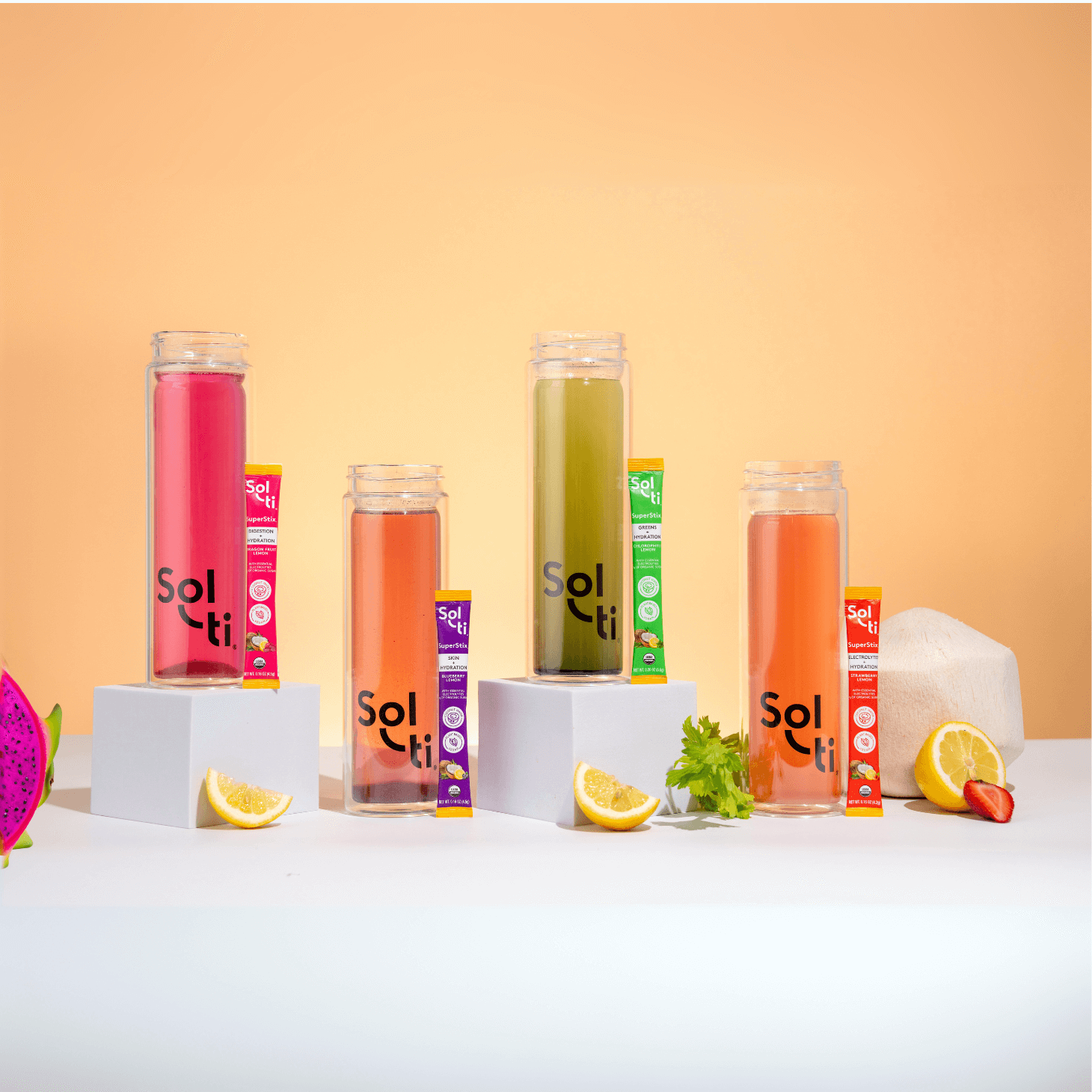 A row of Sol-ti Glass Bottles with SuperStix electrolytes next to a young Coconut, dragon fruit, strawberries, and lemon slices