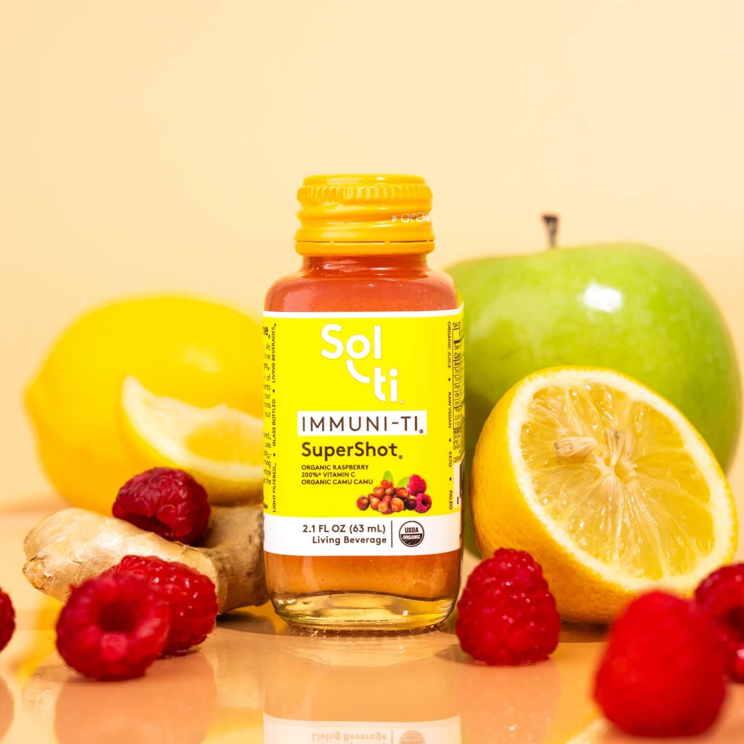 A Sol-ti IMMUNI-TI SuperShot glass bottle with front label next to raspberries, green apples, and lemon slices