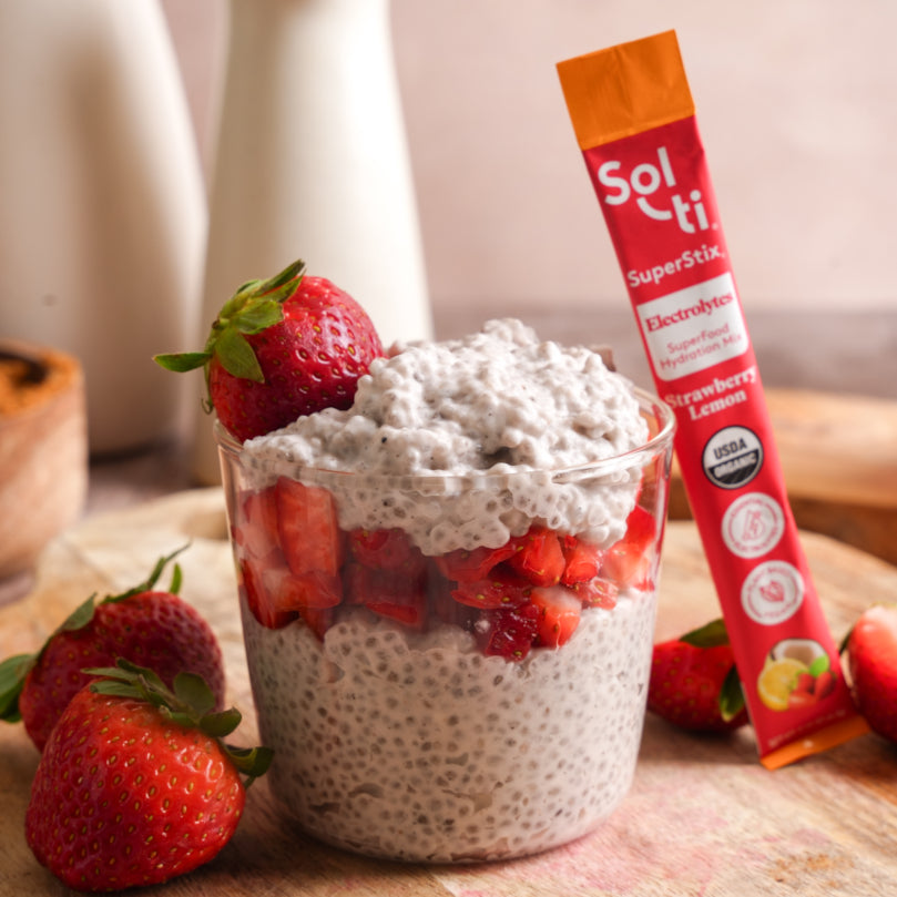 Chia pudding with strawberries and a Sol-ti Strawberry Lemon SuperStix stick on a wooden surface.