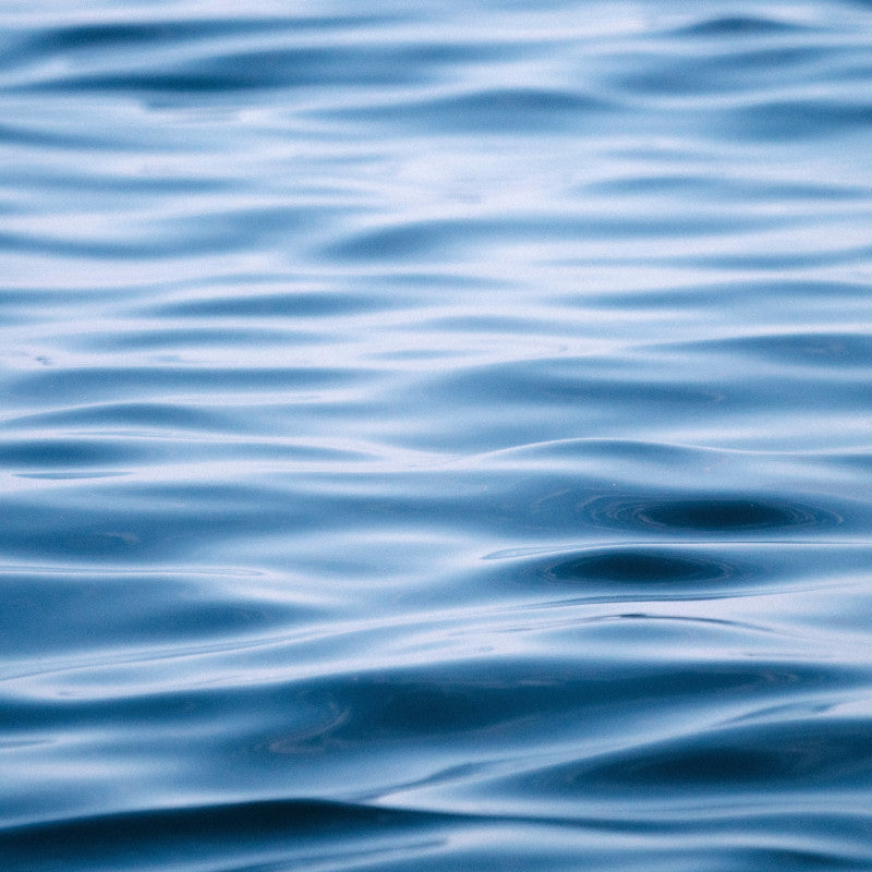 Rippling, deep blue ocean waves with subtle white foam crests, creating a tranquil, wavy texture.