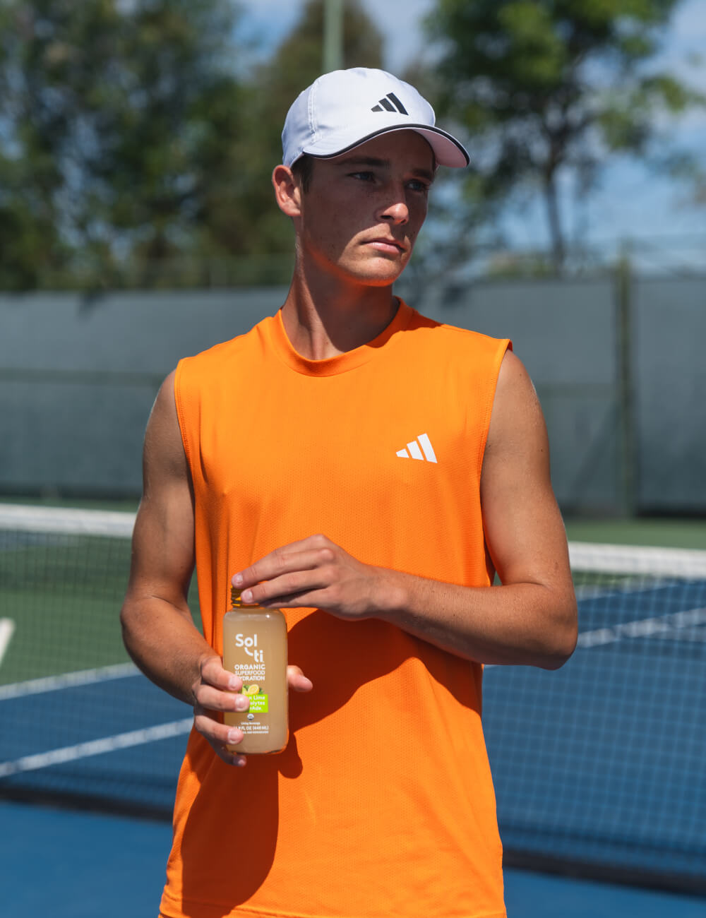 Andy Johnson on a tennis court holding a bottle of Sol-ti Lemon Lime SuperAde