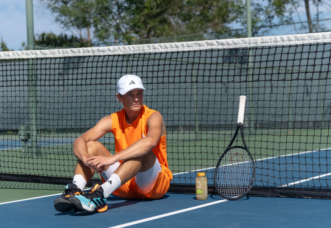 Andy Johnson sits on a blue tennis court net, beside him a Lemon Lime SuperAde bottle