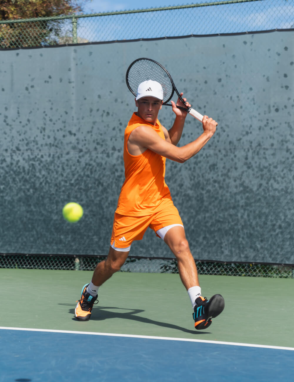 Andy Johnson swings a racket on a blue tennis court, with a yellow tennis ball in mid-air