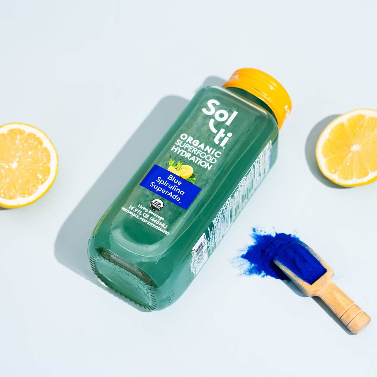 Blue Spirulina SuperAde bottle next to lemons and a spoon of blue spirulina