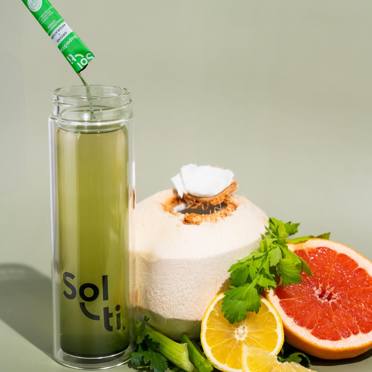 A Sol-ti Glass Bottle with Chlorophyll Lemon SuperStix and water, next to Coconut, grape fruit, celery and lemon slices 