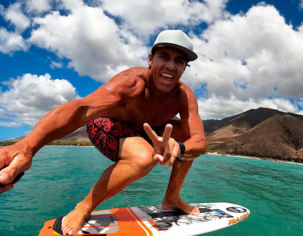 Chuck Patterson crouches on a surfboard in turquoise ocean water 
