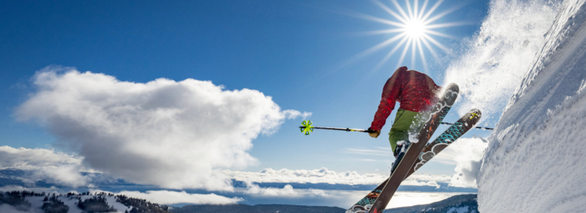 Chuck Patterson jumps off a snowy mountain slope under a bright sun and blue sky with clouds