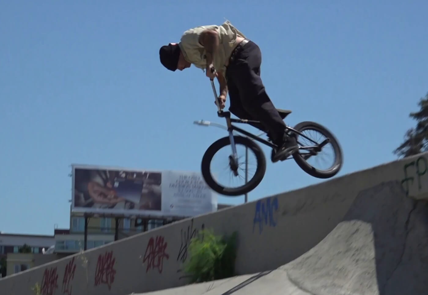 Dakota Roche performs a trick mid-air on a BMX bike at an outdoor skatepark under a clear blue sky