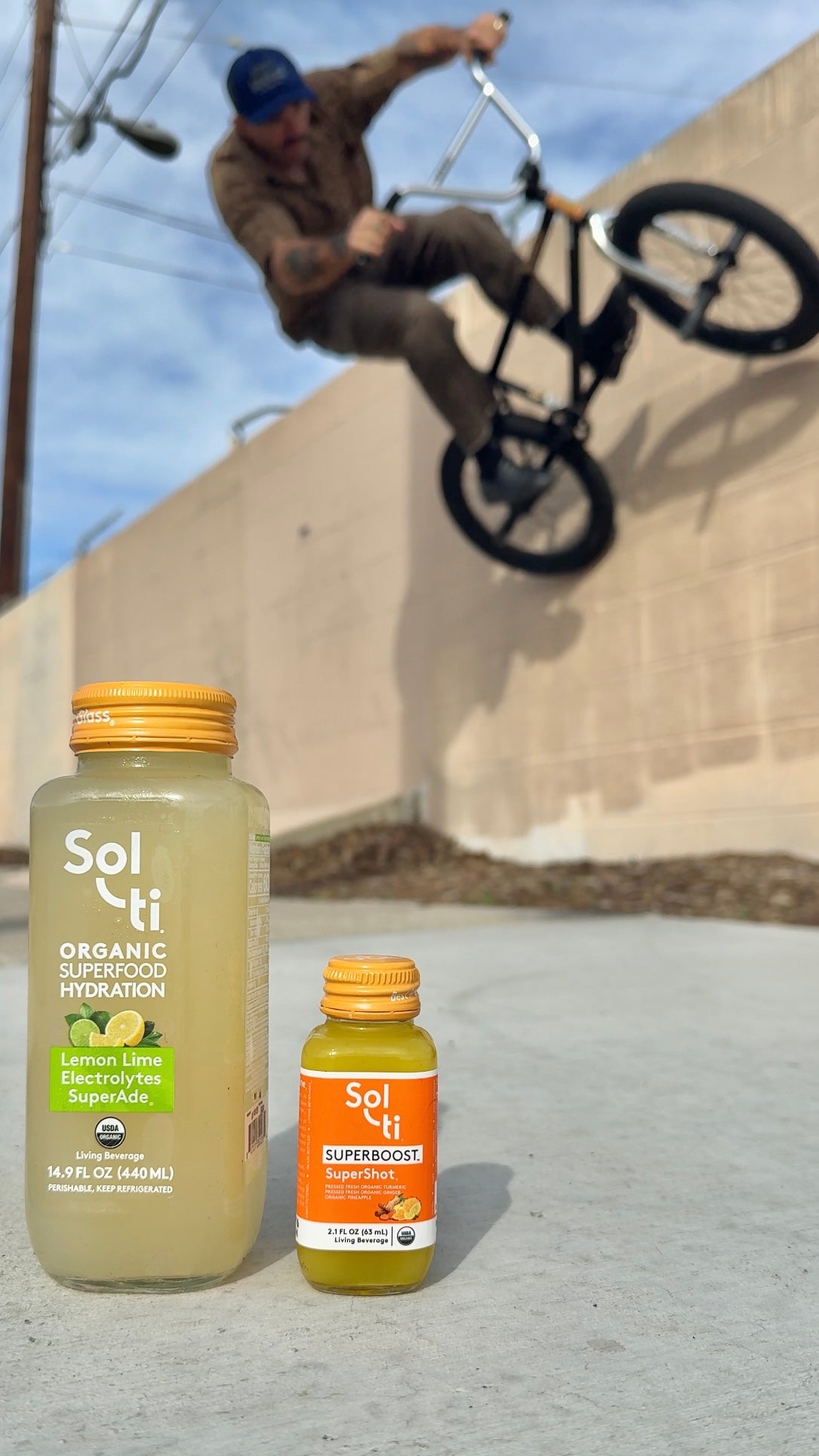 A SuperAde and SuperShot on a concrete surface, with the BMX rider Dakota Roche mid-jump behind