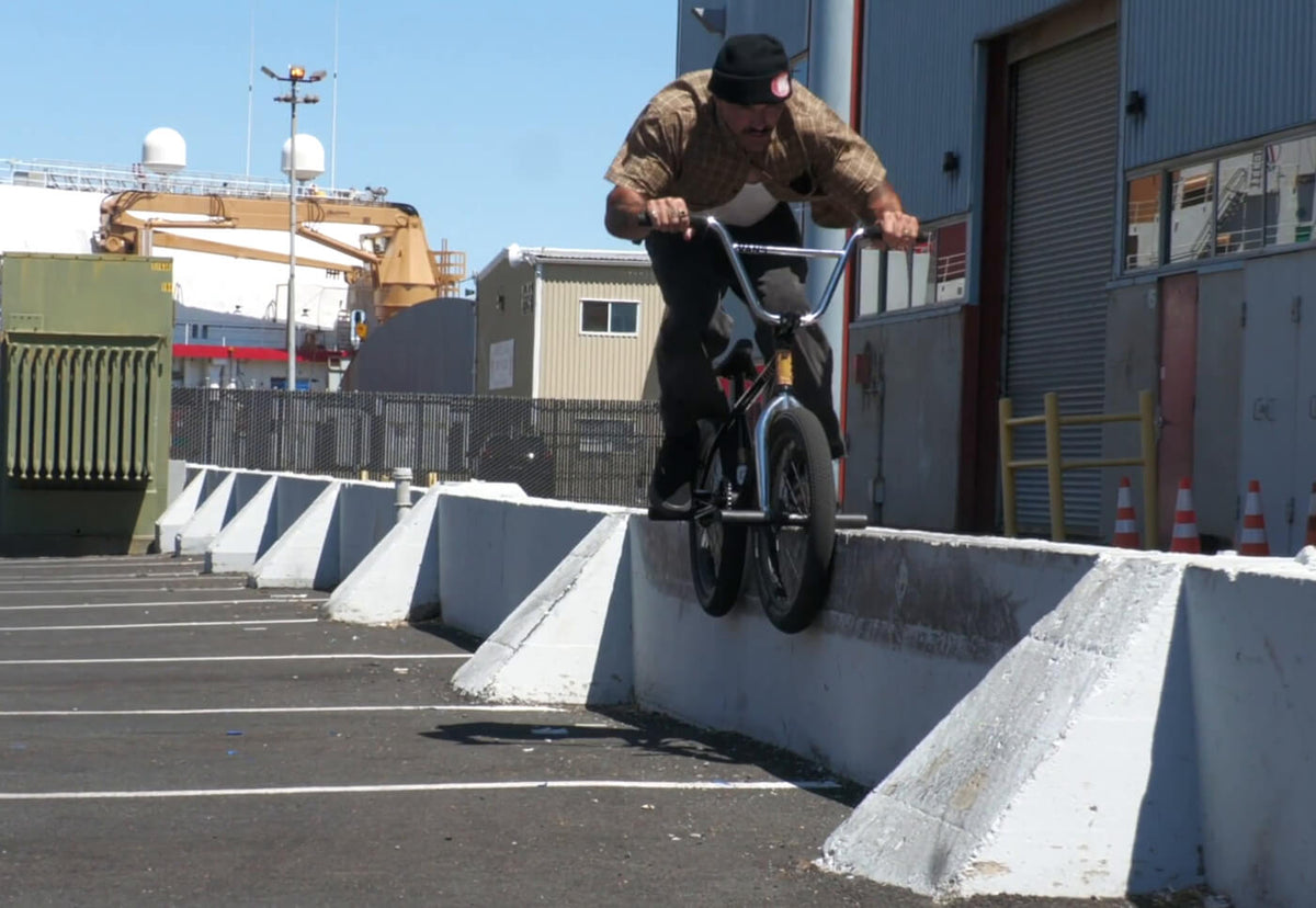 Dakota Roche performs a trick on a concrete barrier in an industrial outdoor setting on a BMX bicycle