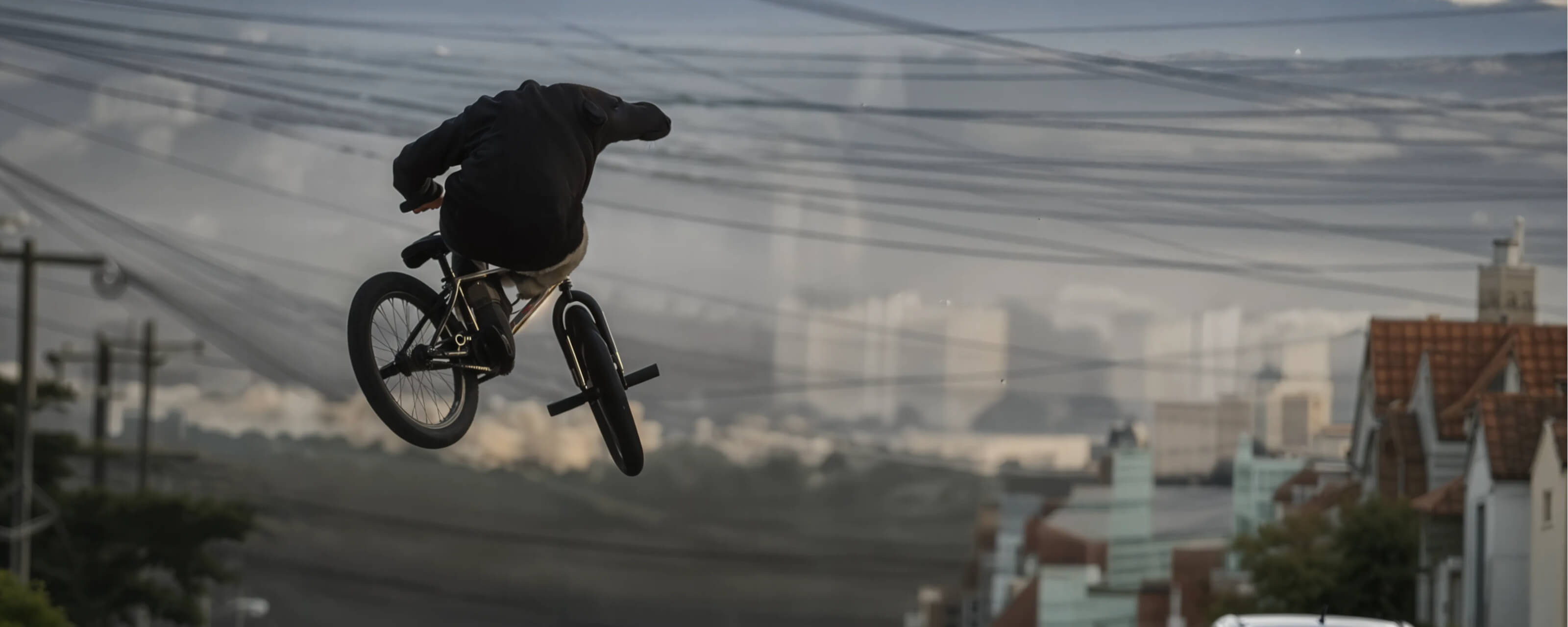 Dakota Roche performs a high jump on a BMX bicycle against a hazy city skyline background