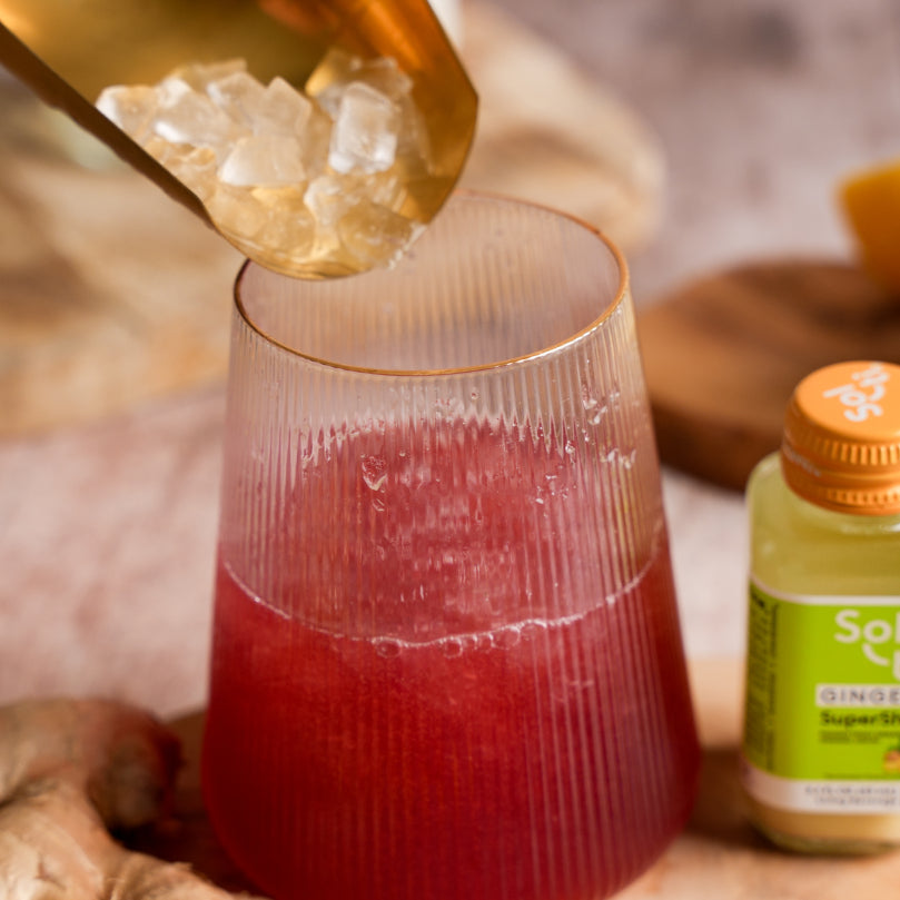 Ice being poured into a glass with Kombucha with a bottle of Sol-ti GINGER SuperShot in the background