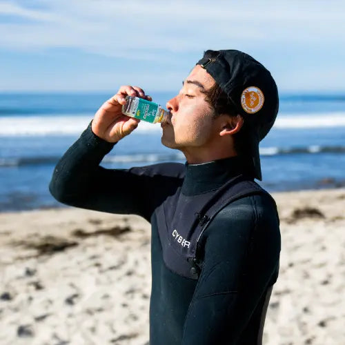 A man on a sandy beach drinks from a ELECTROBOOST SuperShot bottle