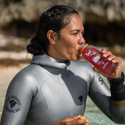 Enchante Gallardo in a gray wetsuit drinking Wild Blueberry SuperAde in the beach
