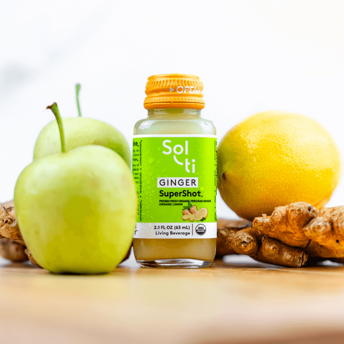 a bottle of GINGER SuperShot next to a lemon, ginger root and a apple