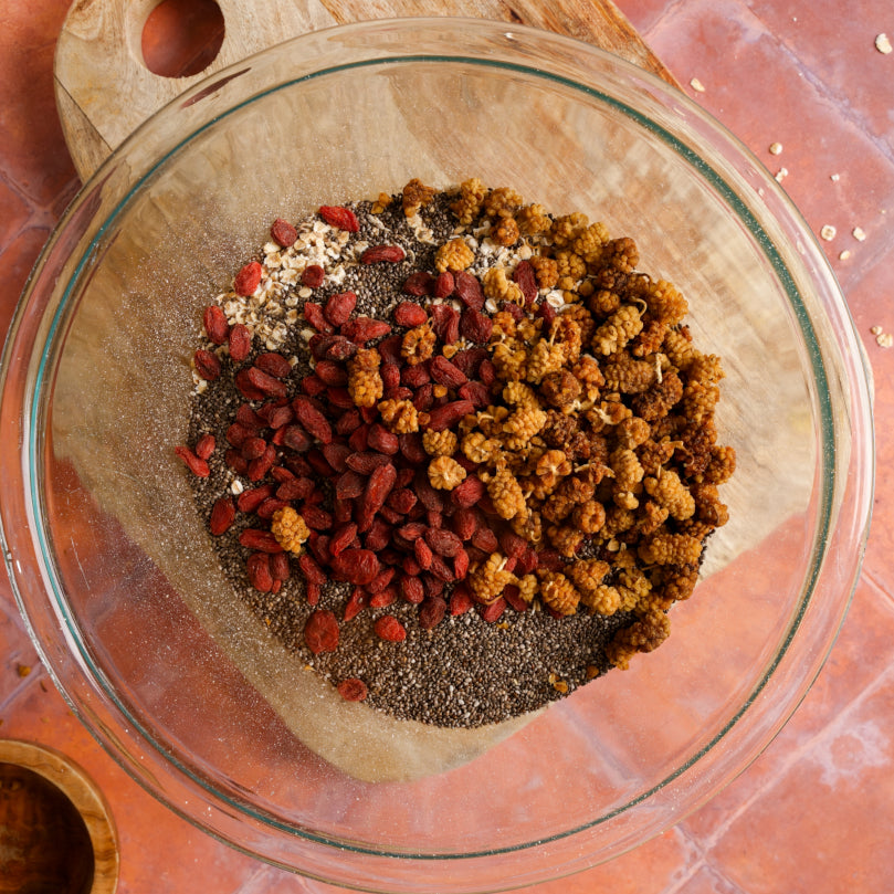 Glass bowl with ground flaxseed, chia seeds, mulberries, rolled oats, and goji berries on a wooden surface