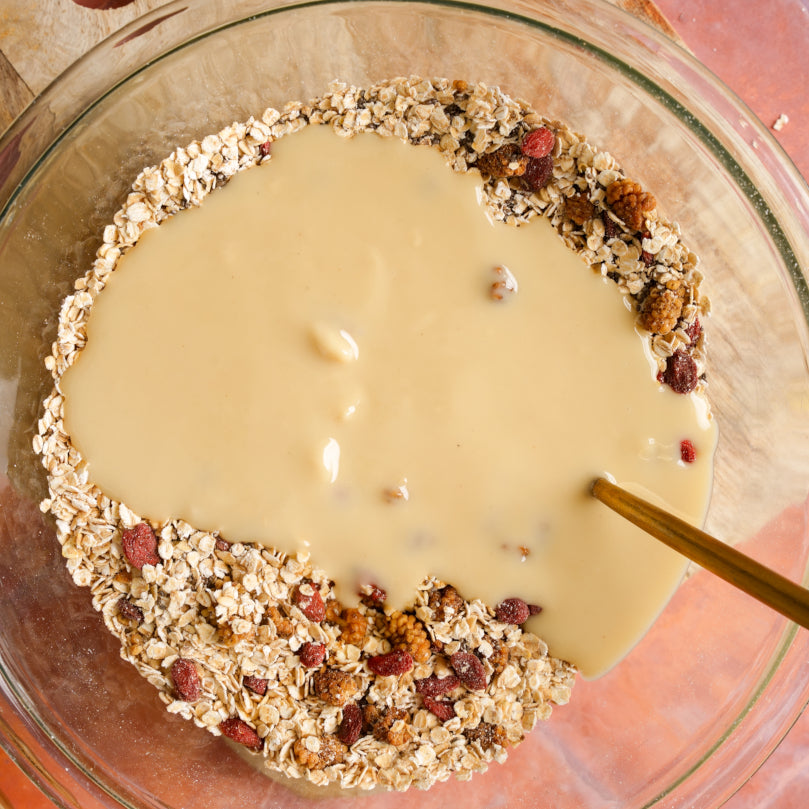 Glass bowl with Nuts and seeds, and  macadamia nut butter being stirred.