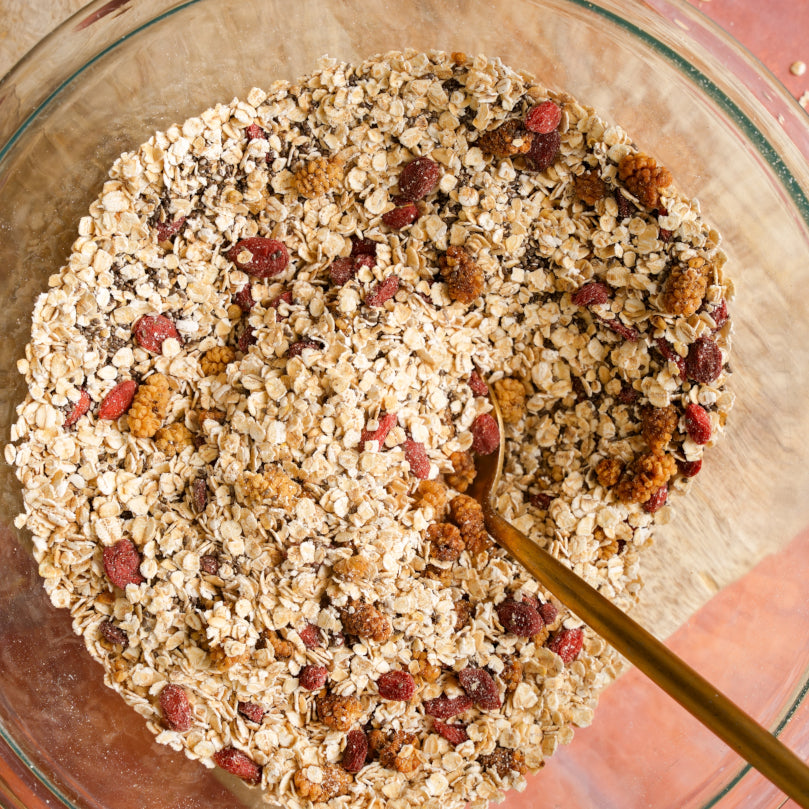 Nuts and seeds in a glass bowl with a gold spoon.
