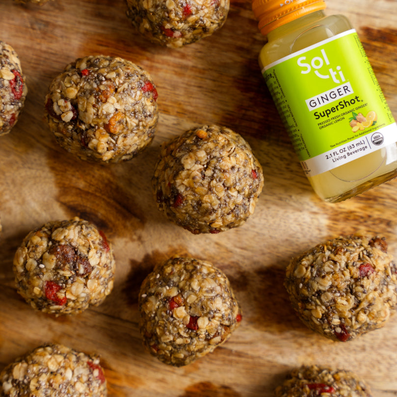 Nuts and seeds balls on a wooden surface with a Bottle of GINGER SuperShot 