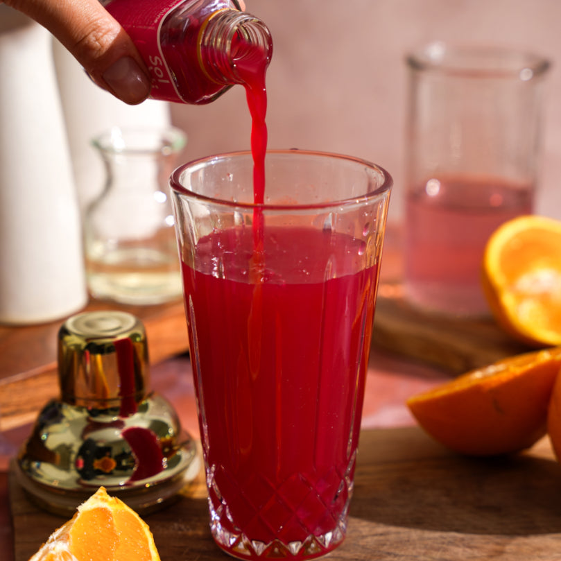 GINGER BEET SuperShot® being poured into a glass with oranges and a bottle in the background.