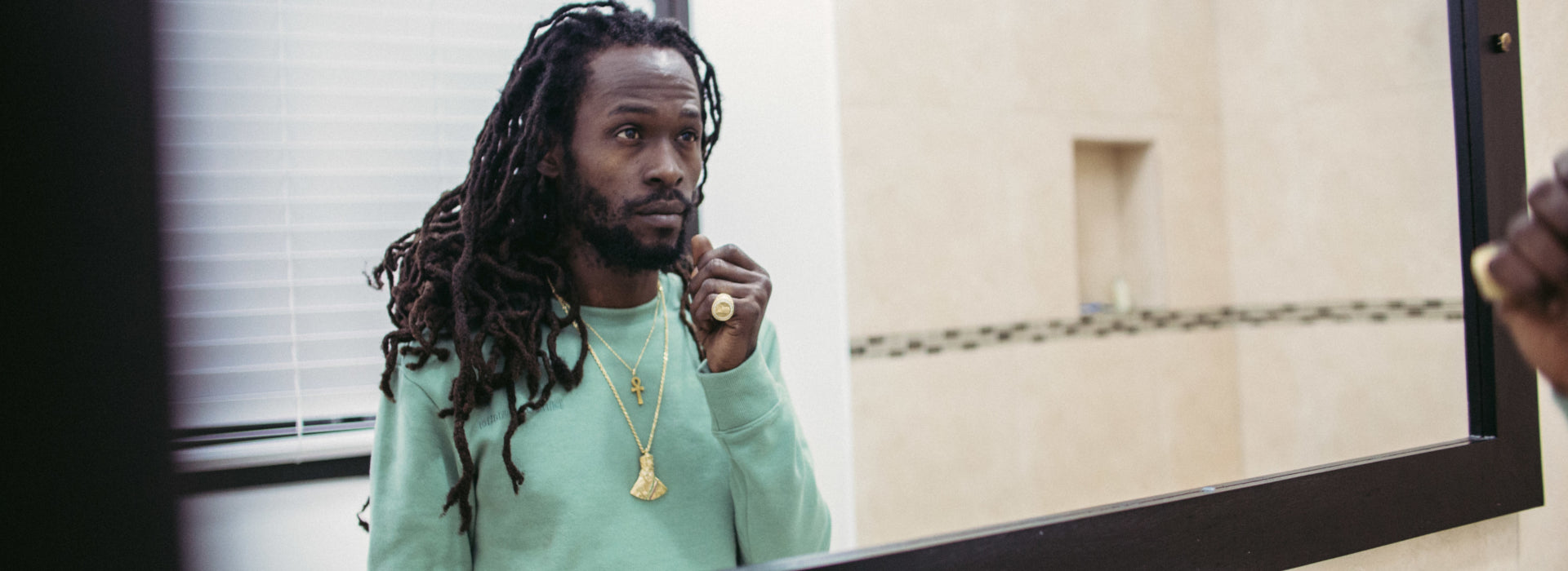 Jesse Royal with long dreadlocks, looking into a mirror 