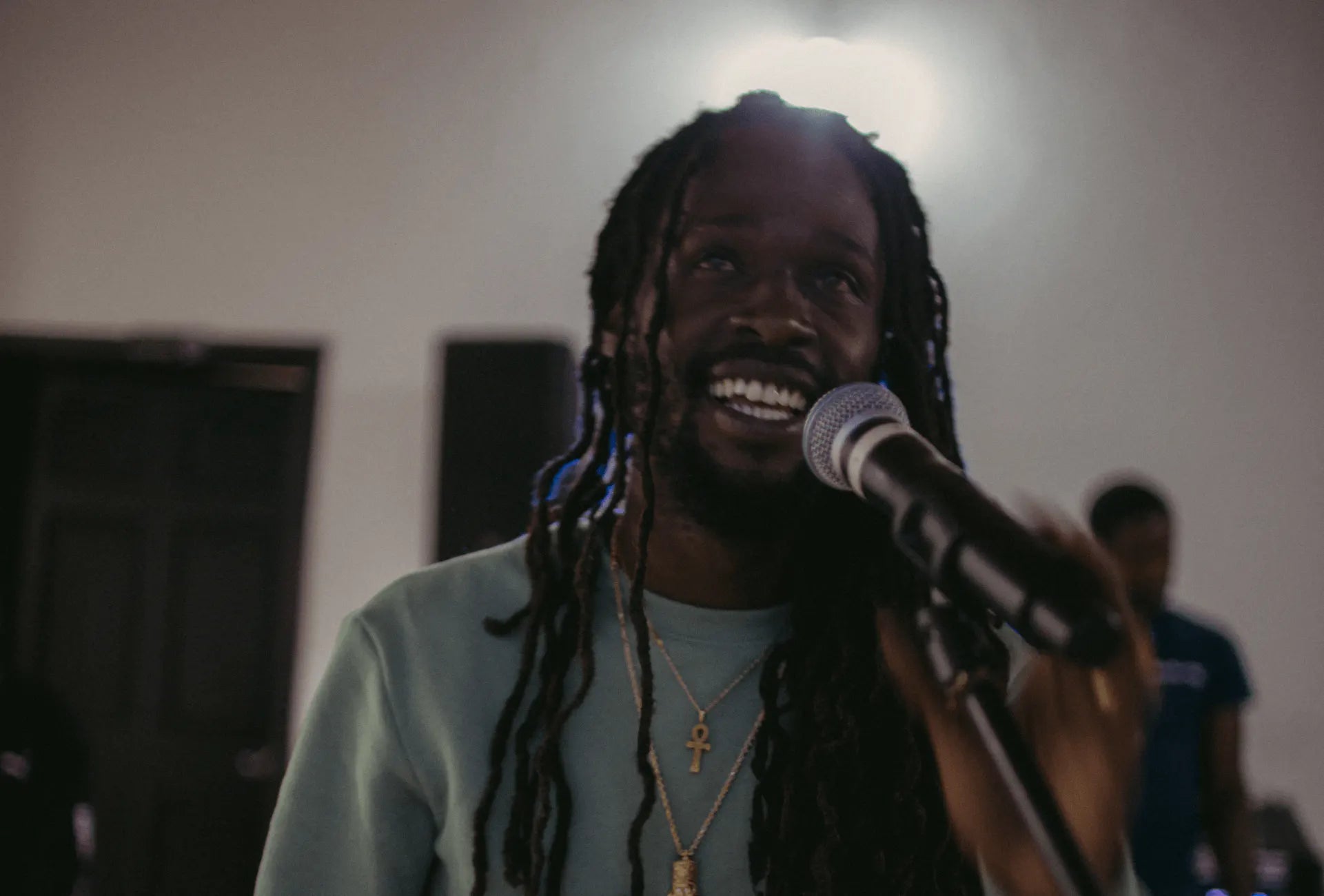 A smiling Jesse Royal sings into a microphone in an indoor setting