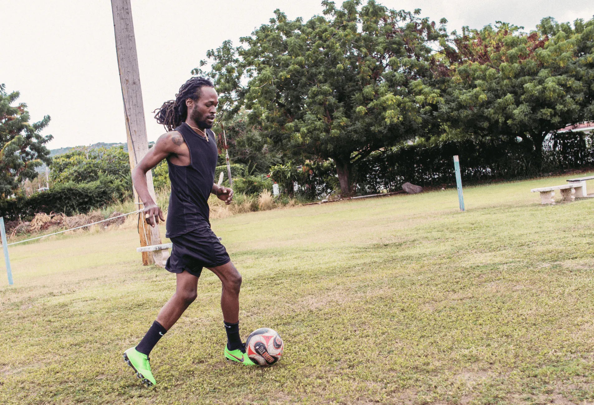 Jesse Royal dribbles a soccer ball on a grassy field with trees
