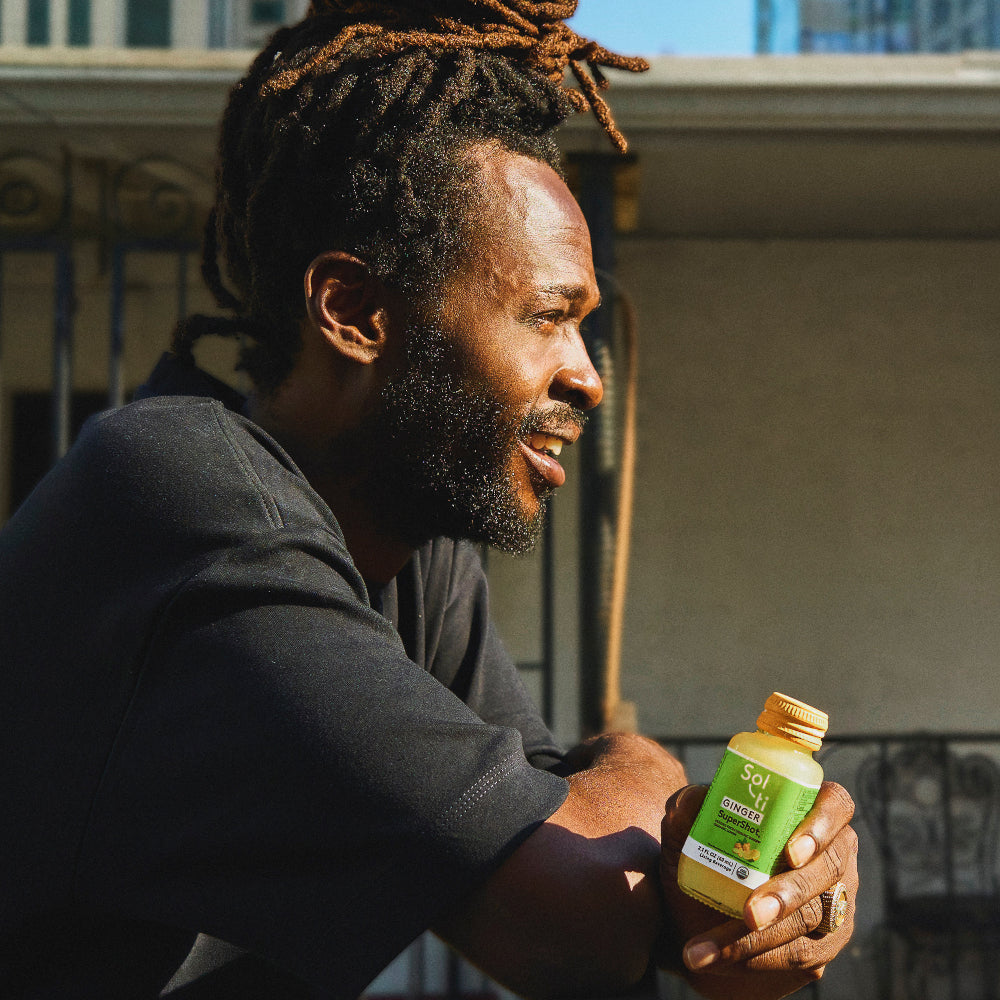 Jesse Royal holds a bottle of GINGER SuperShot in a an outdoor balcony