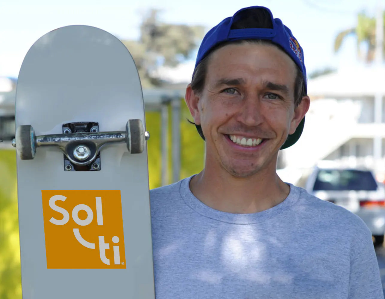 Joey Brezinski smiling holds a white skateboard with orange Sol-ti logo 