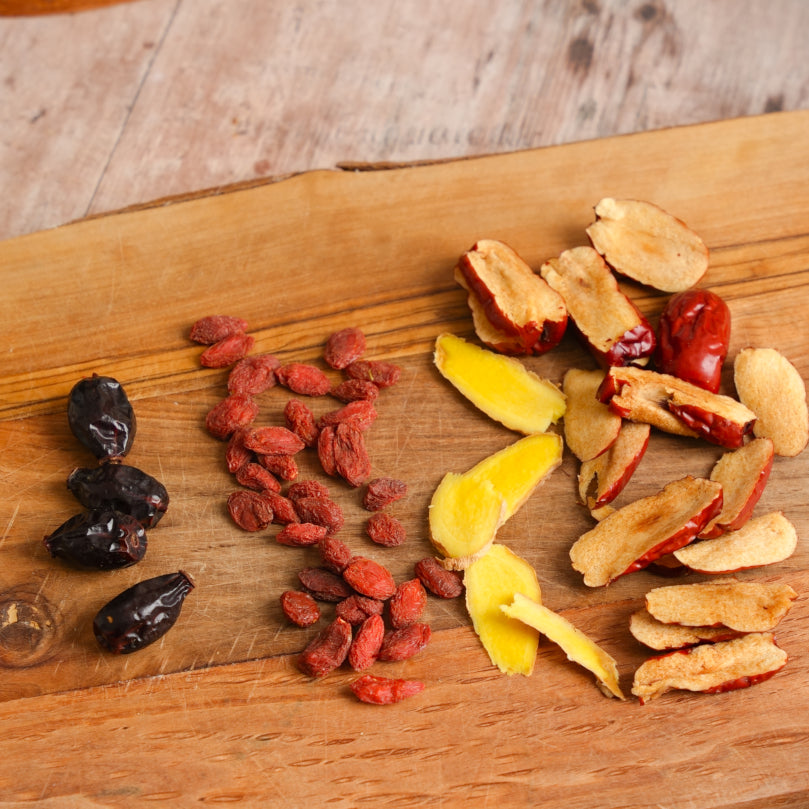 jujubes, goji berries, sliced ginger, and rosehips on a wooden cutting board