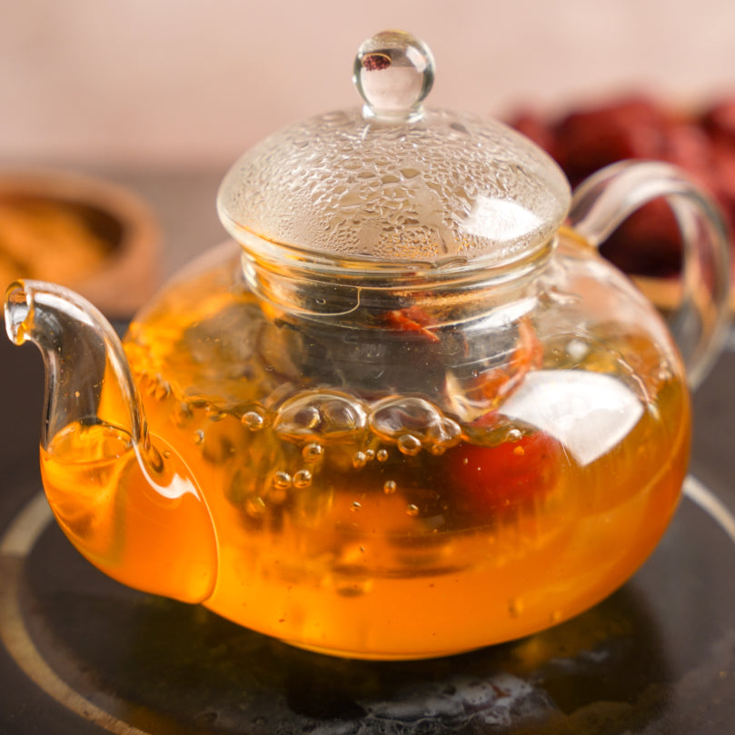 Clear glass teapot with a lid filled with orange tea on a Kitchen.