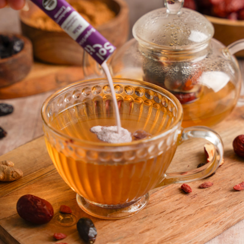 Glass mug being filled with a hot tea and Blueberry Lemon SuperStix on a wooden surface with jujubes.