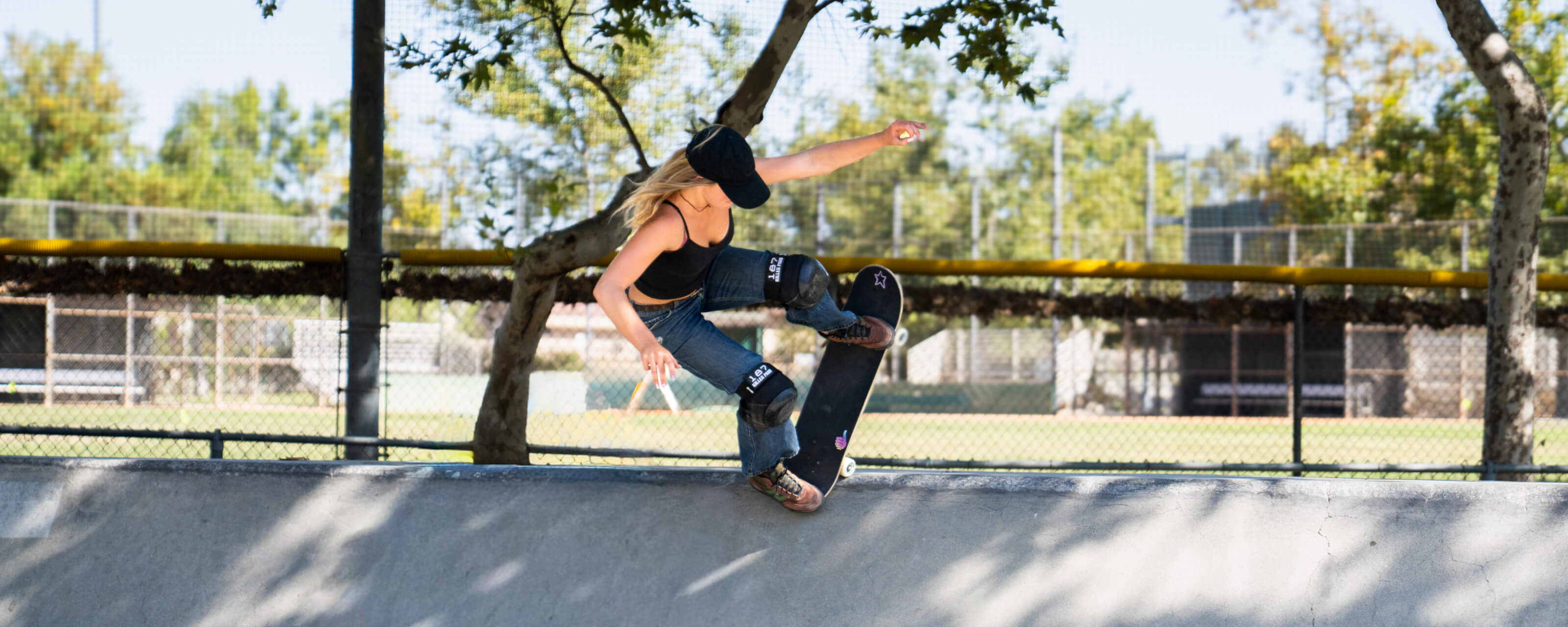Katelyn West is performing a skateboard trick on a concrete ramp at an outdoor skatepark