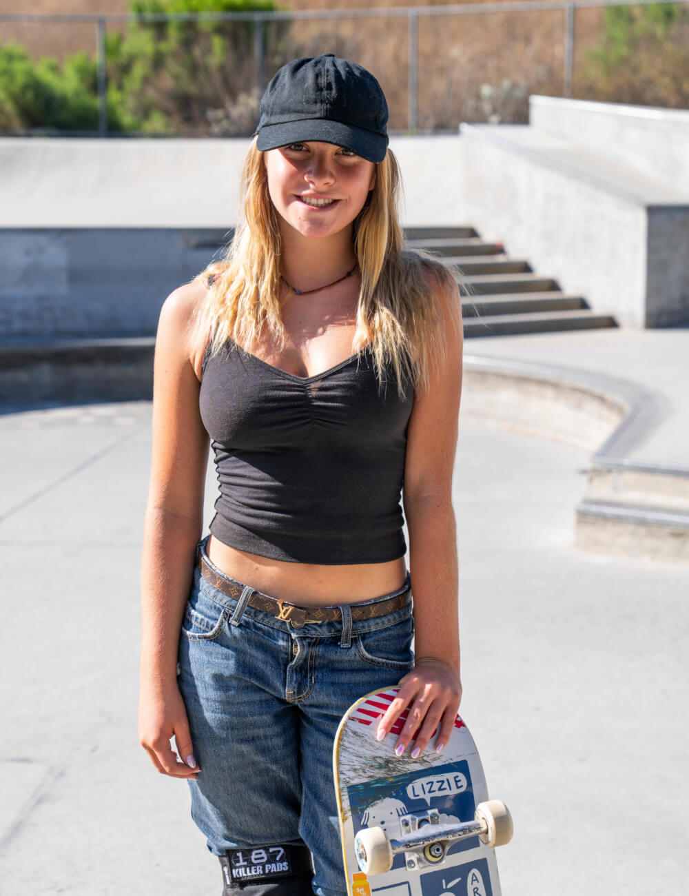 Katelyn West stands at a concrete skatepark holding a skateboard