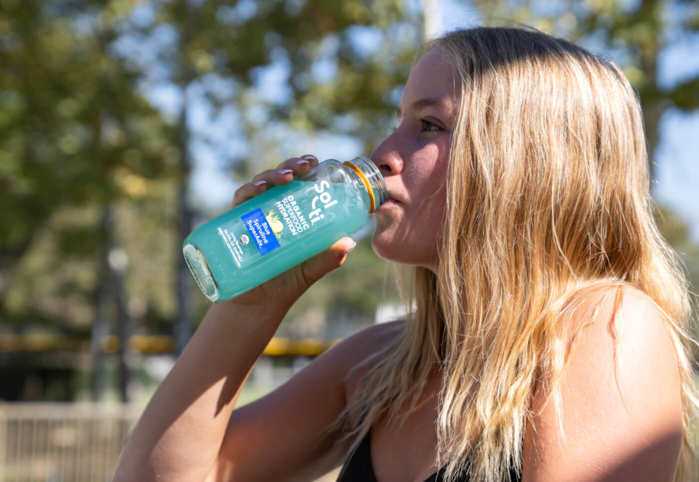 Katelyn West in a sunny outdoor drinking Blue Spirulina SuperAde