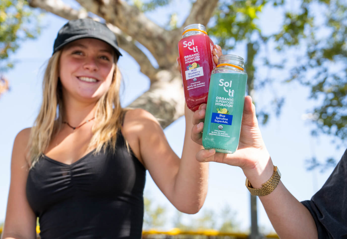 Two people outdoors including Katelyn West holding two SuperAde bottles 