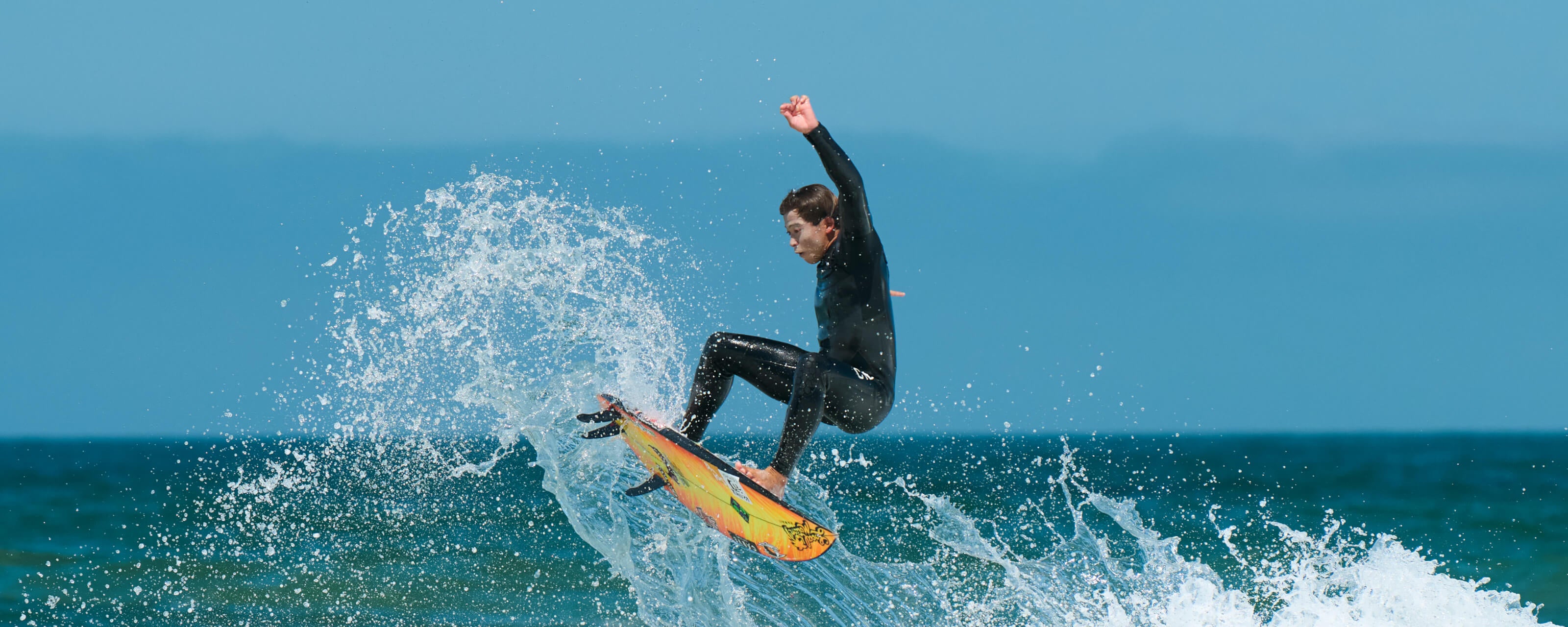 Kei Kovayashi surfing on a wave with a clear blue sky