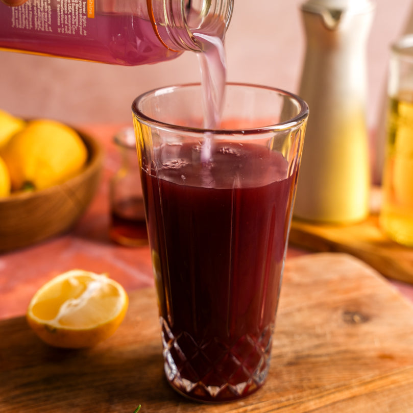Lavender Magnesium SuperAde being poured into a glass on a wooden surface with lemons and a teapot in the background.