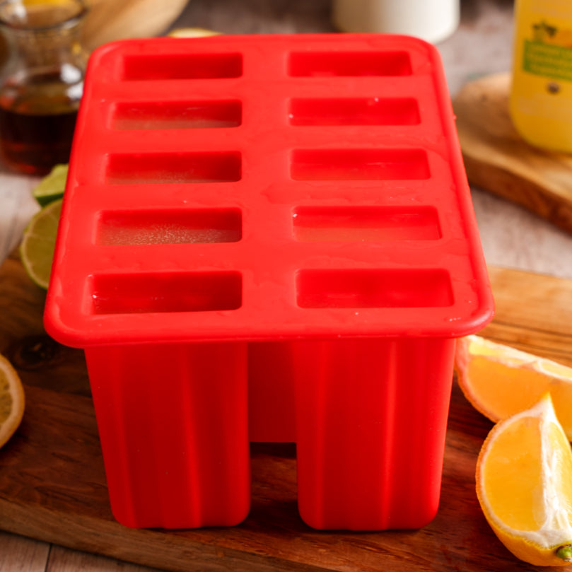 Red silicone popsicle mold on a wooden surface with lemons and a Lemon Lime SuperAde glass bottle in the background.