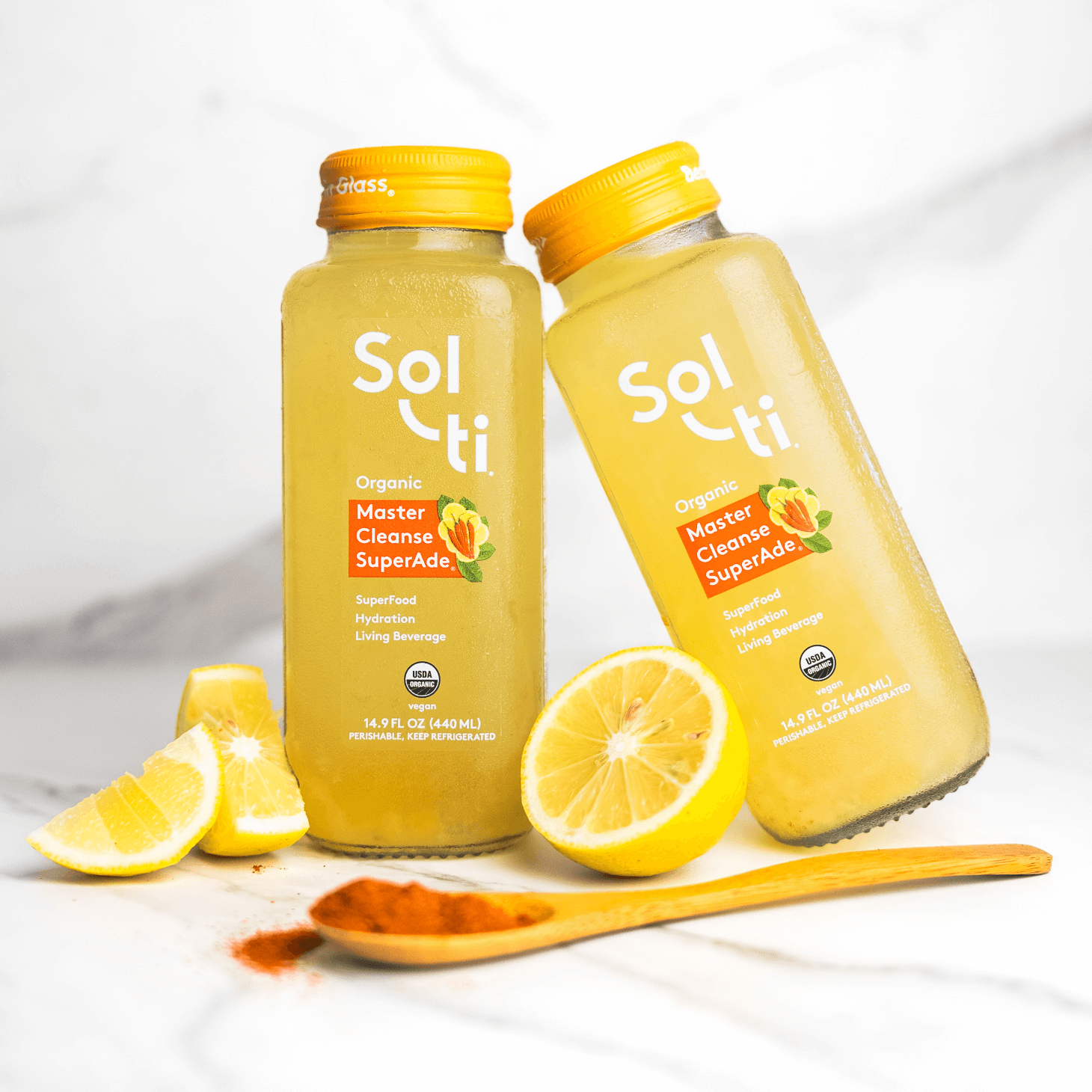 two Master Cleanse SuperAde bottles next to a spoon with cayenne and lemon slices