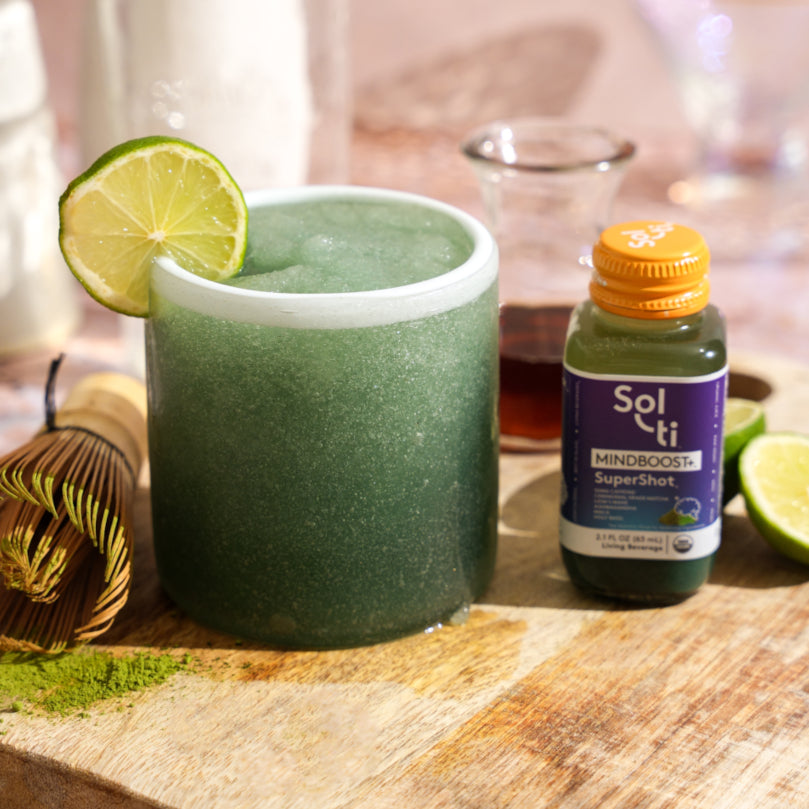 MINDBOOST Slushy with a lemon slice and Sol-ti MINDBOOST+™ SuperShot® bottle on a wooden surface.