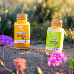 Two SuperShot bottles  TURMERIC and GINGER standing on a stone surface outdoors