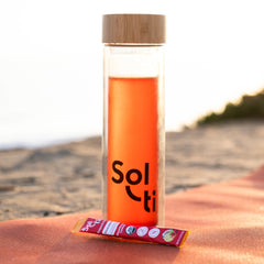 A clear travel tumbler with a bamboo lid, filled with Strawberry Lemon SuperStix with the Solti logo
