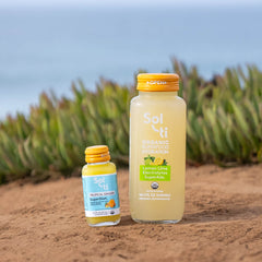 Two Sol-ti bottles Lemon Lime SuperAde and TROPICAL GINGER SuperShot standing on sand