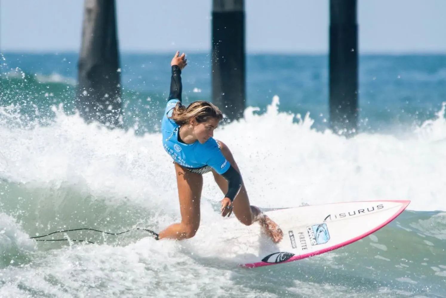 Molly Tuschen surfing on a white wave with pier columns 