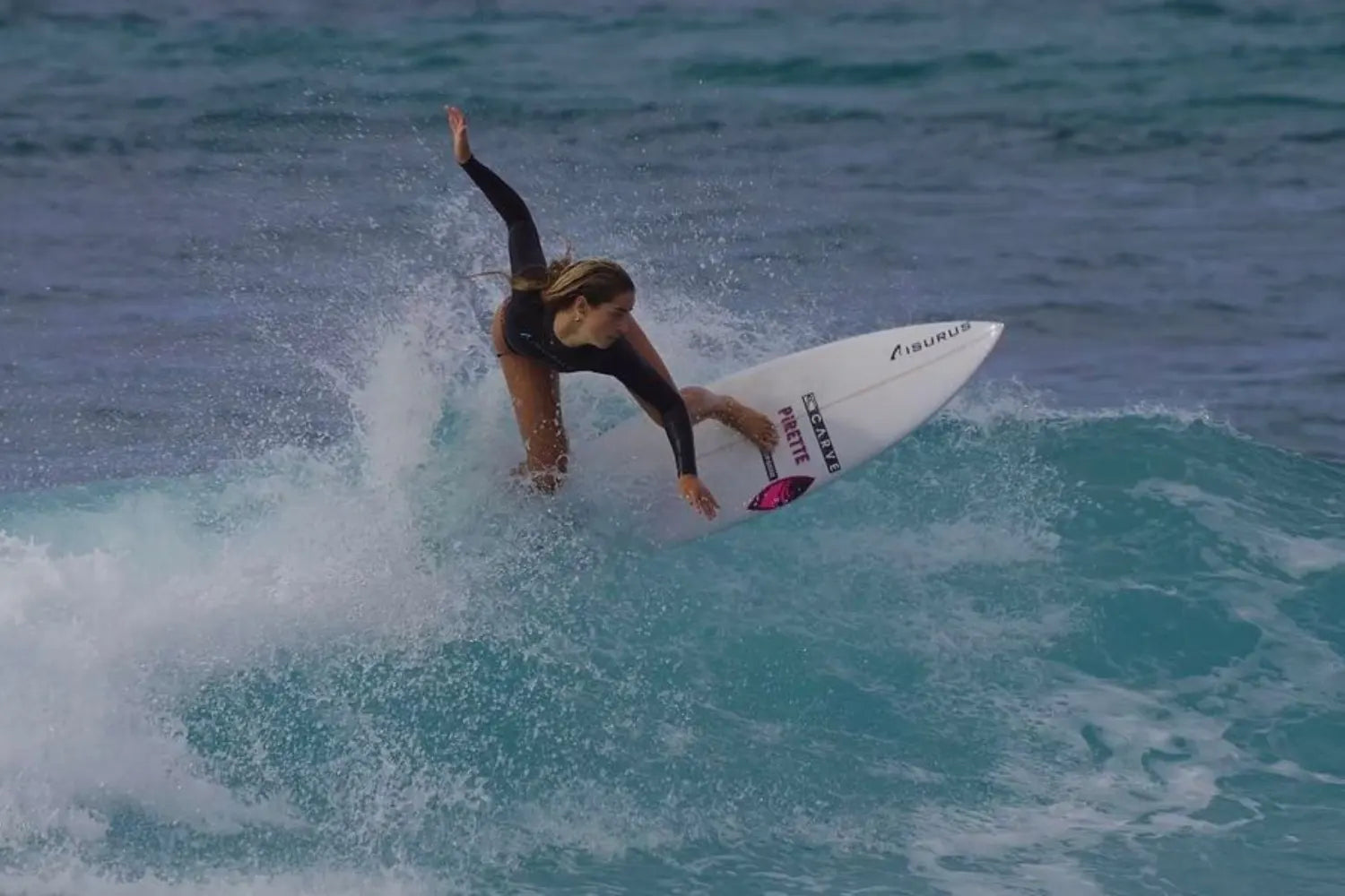 Molly Tuschen rides a surfboard on a turquoise ocean wave